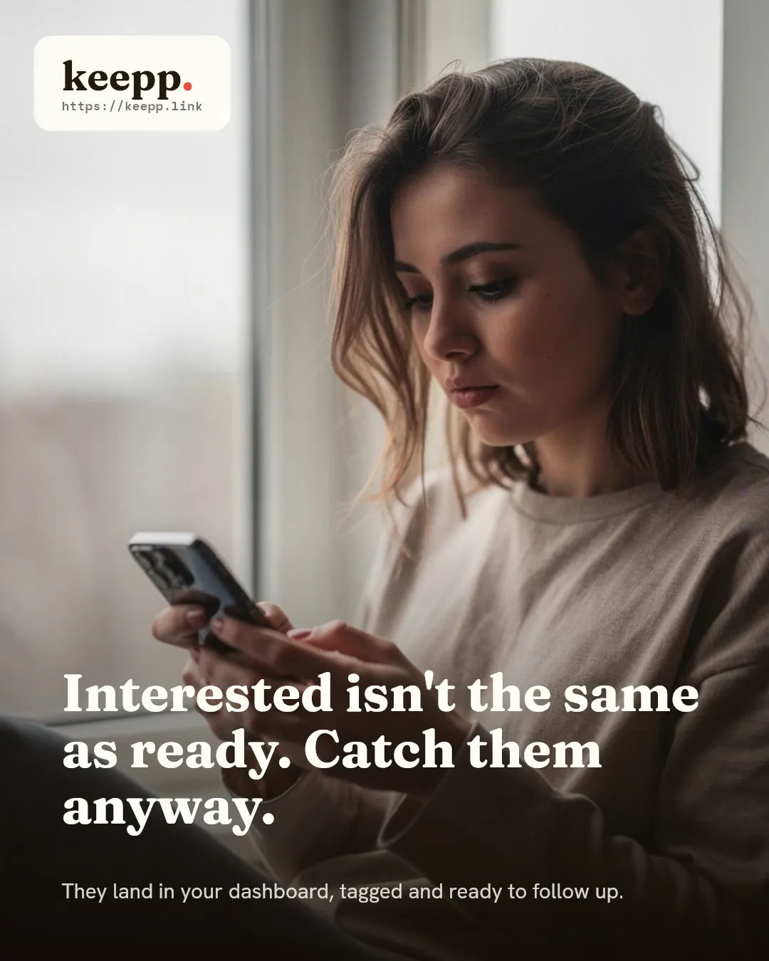 A woman by a window scrolling her phone with a thoughtful, undecided expression